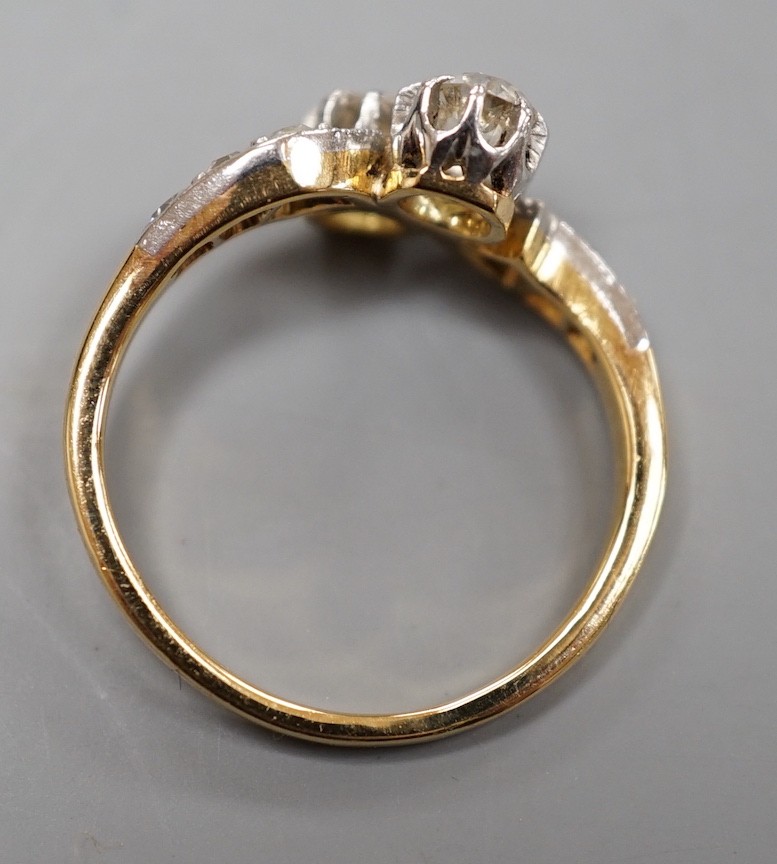 A yellow metal and two stone diamond set crossover ring, with diamond set shoulders, size J, gross weight 3.1 grams.